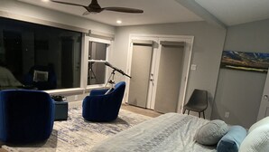 Ein Schlafzimmer mit einem Bett, einem blauen Sessel, einem Schreibtisch mit einem Mikrofon und einem großen Fenster.