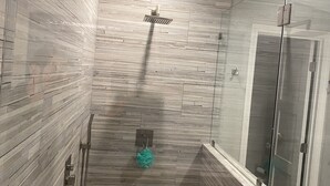 Eine moderne Dusche mit Regendusche, Glastür und Boden in Kieselsteinoptik.