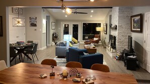 Ein geräumiges Wohnzimmer mit Kamin, einem Essbereich mit Holztisch und einer Küche im Hintergrund.