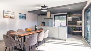 A modern kitchen with a central island, a dining area with a wooden table and cushioned chairs, and a large window providing natural light. - Luxurious villa with private pool and sun terrace (Valbandon)