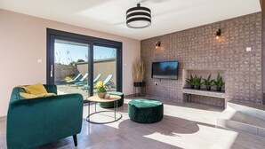 A modern living room with a large TV, comfortable seating, a fireplace, and a balcony with sun loungers. - Luxurious villa with private pool and sun terrace (Valbandon)