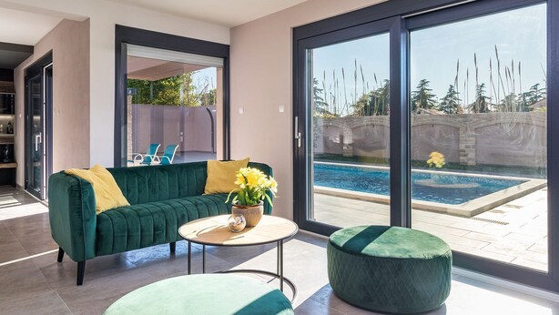 A modern living room with a green sofa, a round coffee table, and a view of a swimming pool through large glass doors. - Luxurious villa with private pool and sun terrace (Valbandon)
