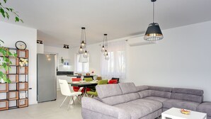 A modern living room with a grey sectional sofa, a dining area with a table and chairs, and a kitchen in the background. - Modern villa with private pool, sun terrace only 2 km from the beach (Medulin)