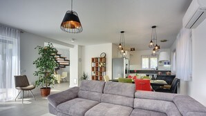A modern living room with a grey sectional sofa, a dining area with a table set for four, and a staircase leading to an upper floor. - Modern villa with private pool, sun terrace only 2 km from the beach (Medulin)