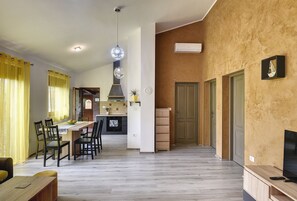 Une cuisine moderne dotée d’un îlot central, un coin repas avec des rideaux jaunes et un espace de vie comprenant un téléviseur et une télécommande.
