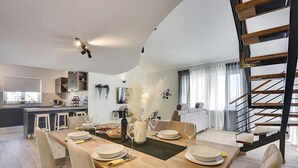 A modern kitchen with a central island, a dining area with a wooden table set for four, and a staircase with a wooden finish. - Modern holiday flat with balcony, BBQ, WLAN, air conditioning (Vodnjan)