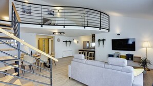 A modern living room with a curved staircase, a sofa, a TV, and a dining area. - Modern holiday flat with balcony, BBQ, WLAN, air conditioning (Vodnjan)