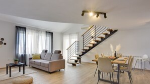 A modern living room with a sofa, a dining table set for two, and a staircase leading to an upper floor. - Modern holiday flat with balcony, BBQ, WLAN, air conditioning (Vodnjan)