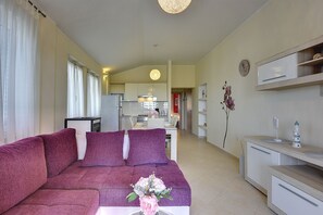 A living room with a purple sofa, a dining area, a kitchen, and a bathroom with a mirror and a clock.