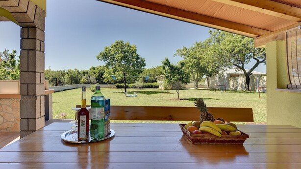 An outdoor patio with a wooden table, a bench, and a view of a grassy yard with trees. - Holiday home with badminton and mini football pitch (Pula)