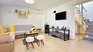 A modern living room with a sofa, coffee table, and ottomans, a fireplace, and a staircase leading to an upper level. - Holiday home with badminton and mini football pitch (Pula)