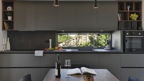 A modern kitchen with a built-in oven, a window with a view of greenery, and a dining area with a table and chairs. - 700 metres to the beach with private pool, WiFi, sea view (Medulin)