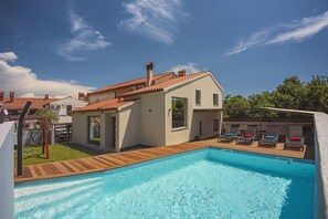 A modern house with a swimming pool, a wooden deck, and a covered outdoor seating area.