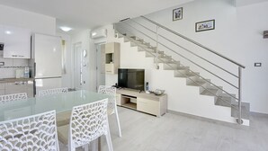 Eine moderne Küche mit weißen Schränken, einem Glastisch und einer Treppe mit Metallgeländer.
