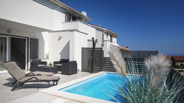Ein moderner Poolbereich im Freien mit Liegestühlen und einem Patio-Tisch, umgeben von einem weißen Gebäude mit einem Balkon.