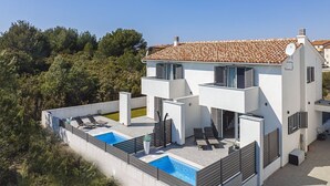 Ein modernes, zweistöckiges Haus mit Swimmingpool, einer Terrasse mit Liegestühlen und Blick auf die umliegende Natur.