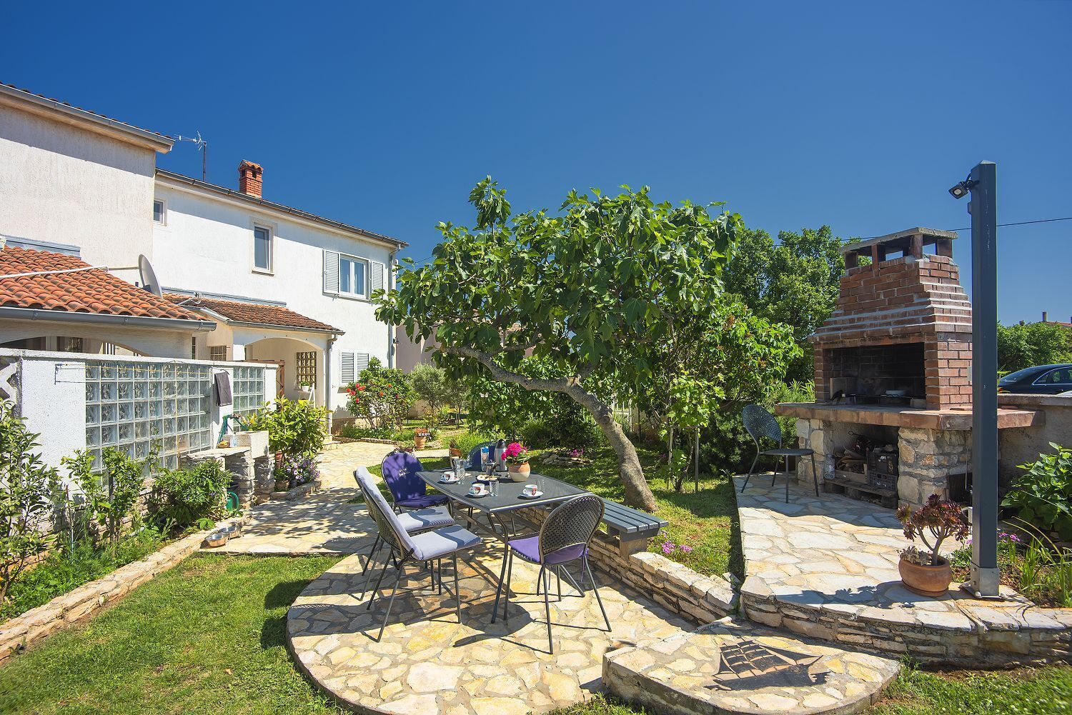 Une terrasse avec une table et des chaises, un four en briques et un bâtiment blanc avec un toit en tuiles.