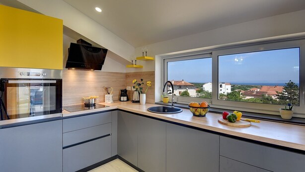 Una cucina moderna con forno integrato, lavello e finestra con vista sul mare e sugli edifici.