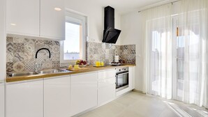 A modern kitchen with white cabinets, a black range hood, a window with a view, and a large sliding glass door. - Villa with private pool, playground, WiFi, air conditioning, BBQ (Pula)