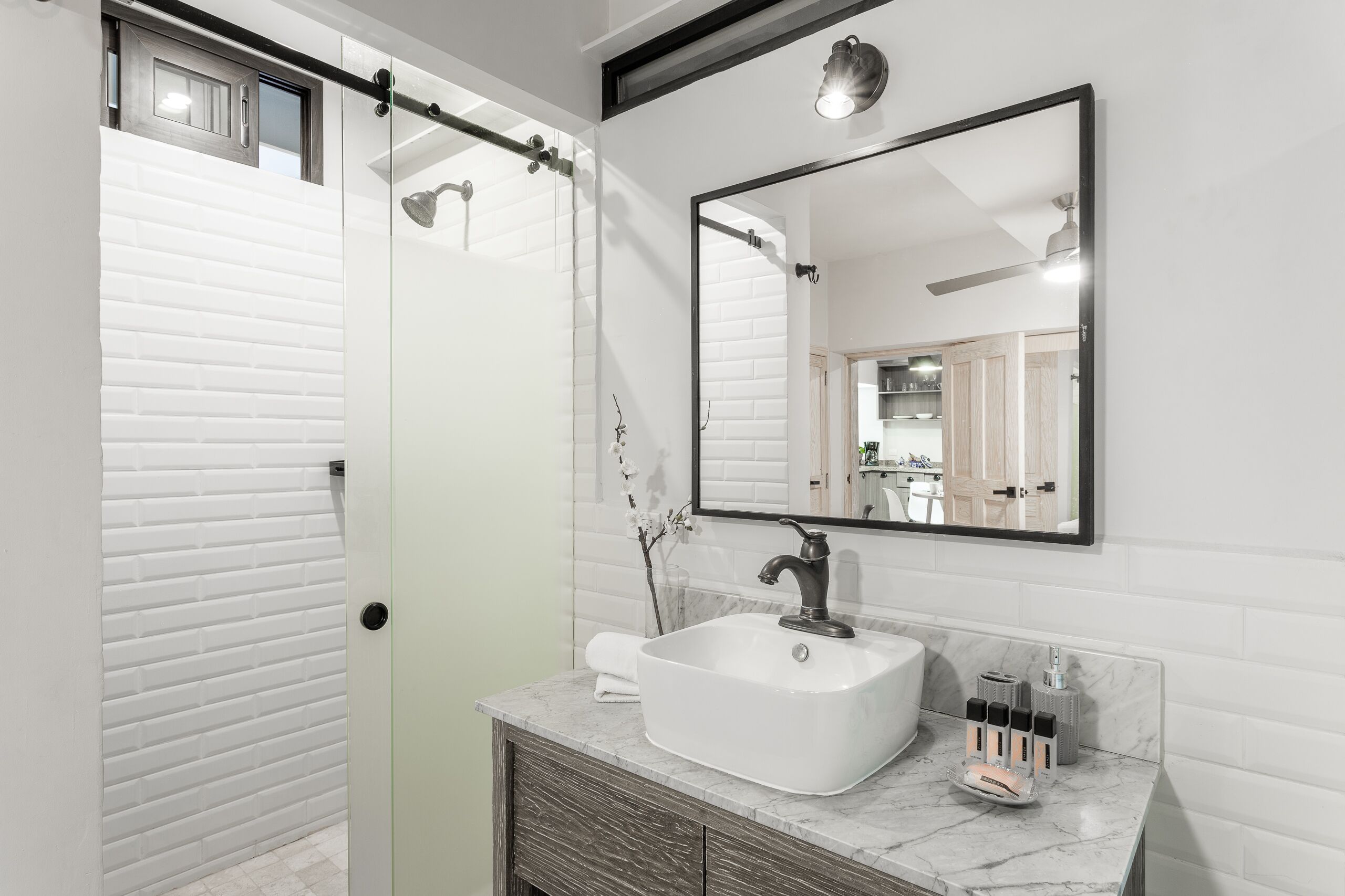 A modern bathroom with a glass shower enclosure, a white sink with a marble countertop, and a large mirror above the sink.