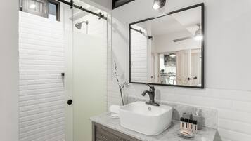 A modern bathroom with a glass shower enclosure, a white sink with a marble countertop, and a large mirror above the sink.