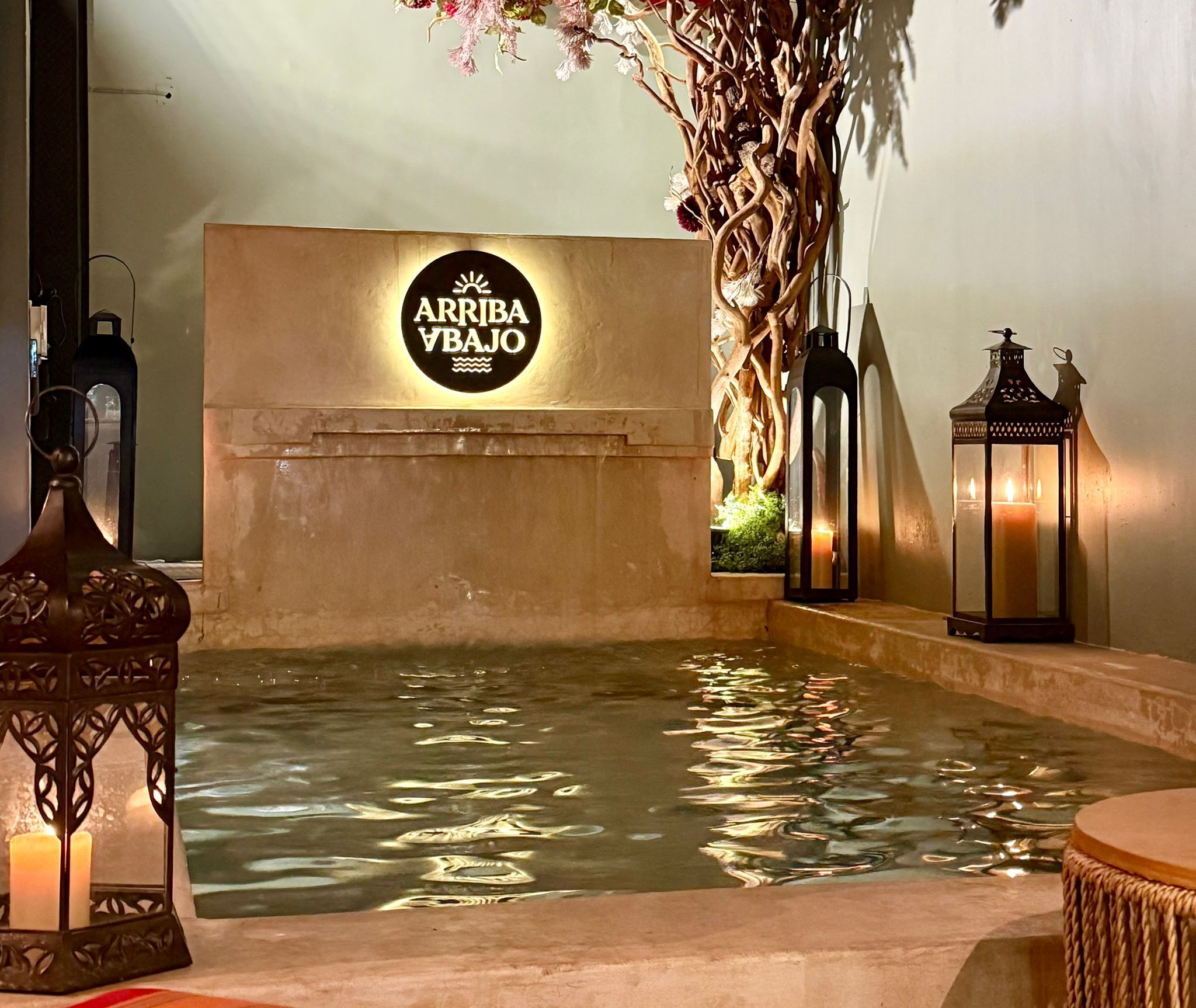 Een wellnessruimte met een bord waarop 'ARRIBA YBAJO' staat, een waterpartij en decoratieve lantaarns.