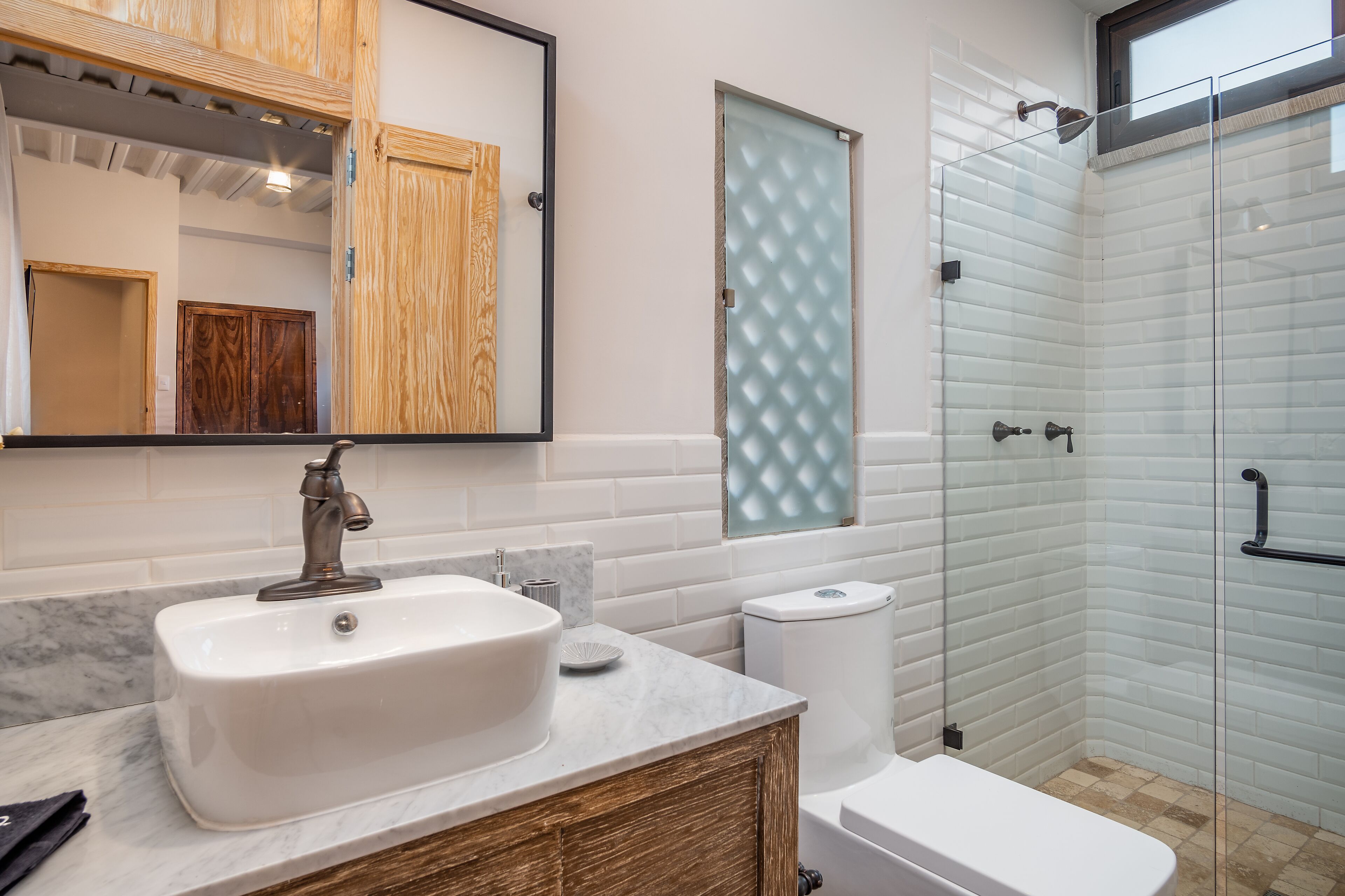 A bathroom with a white sink, wooden cabinets, a glass shower enclosure, and a marble countertop.
