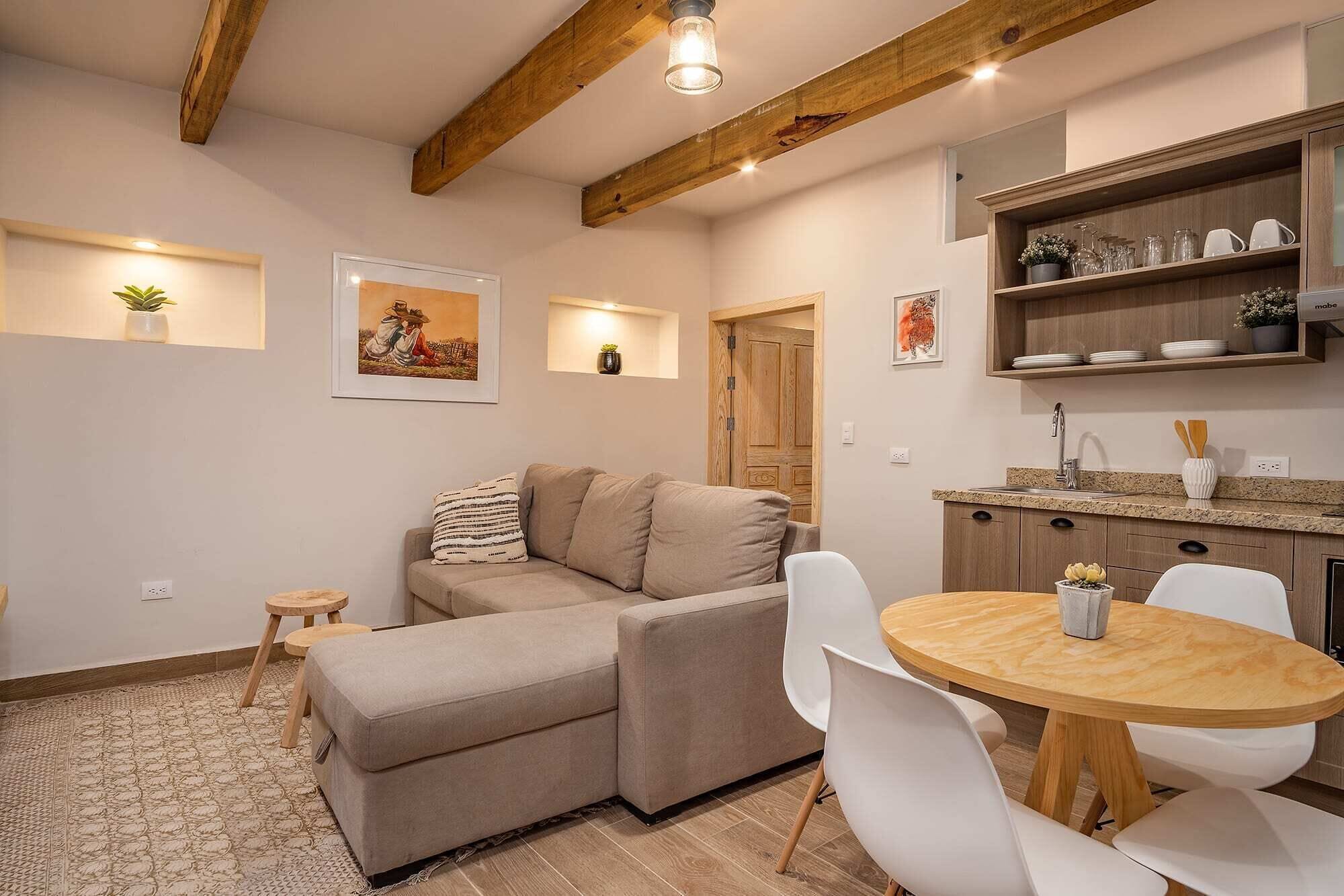 Una sala de estar acogedora con un sofá, una mesa de comedor con sillas y una cocina con armarios de madera y un lavabo.