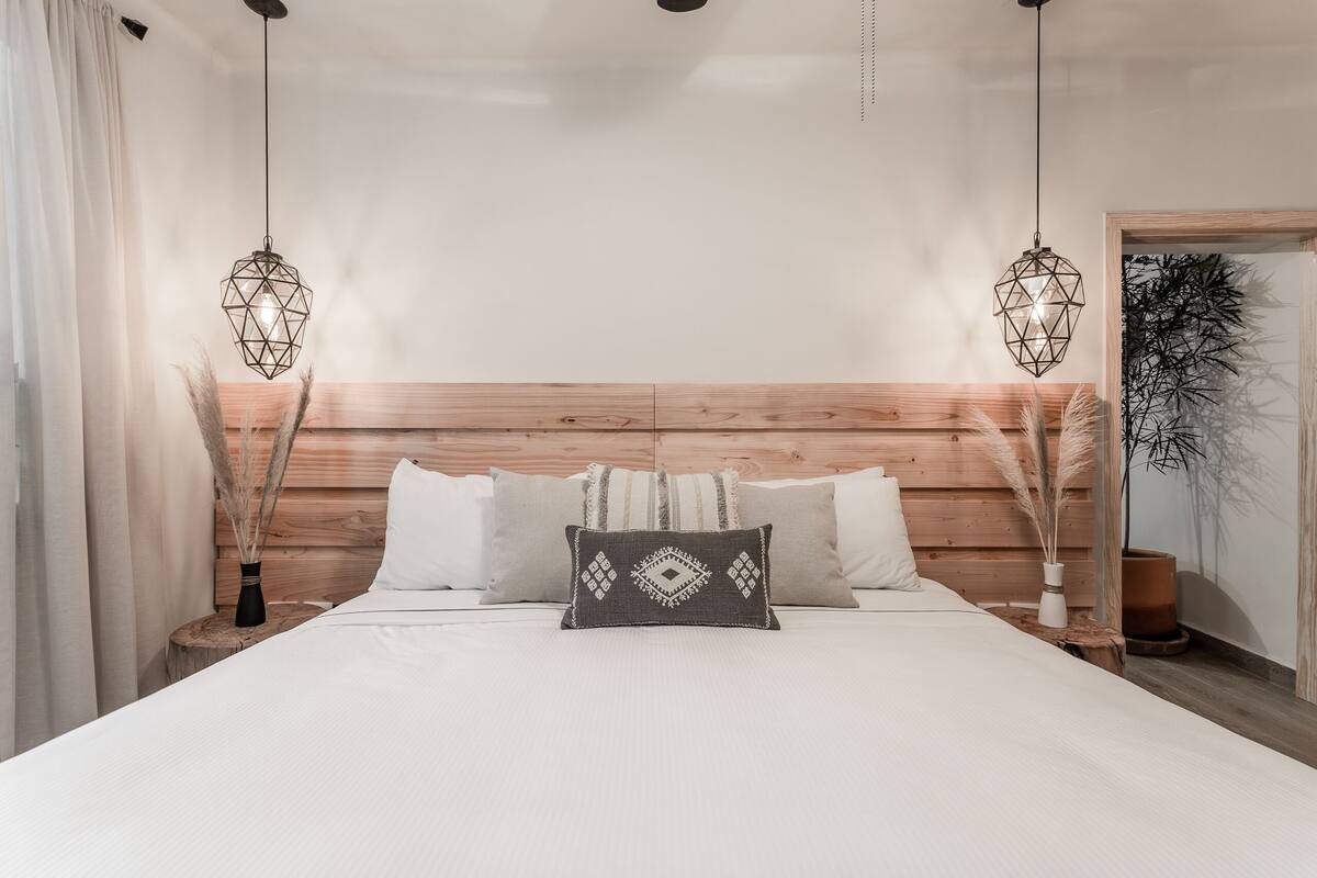 Een slaapkamer met een houten hoofdbord, een wit beddegoed en twee hangende lampen.