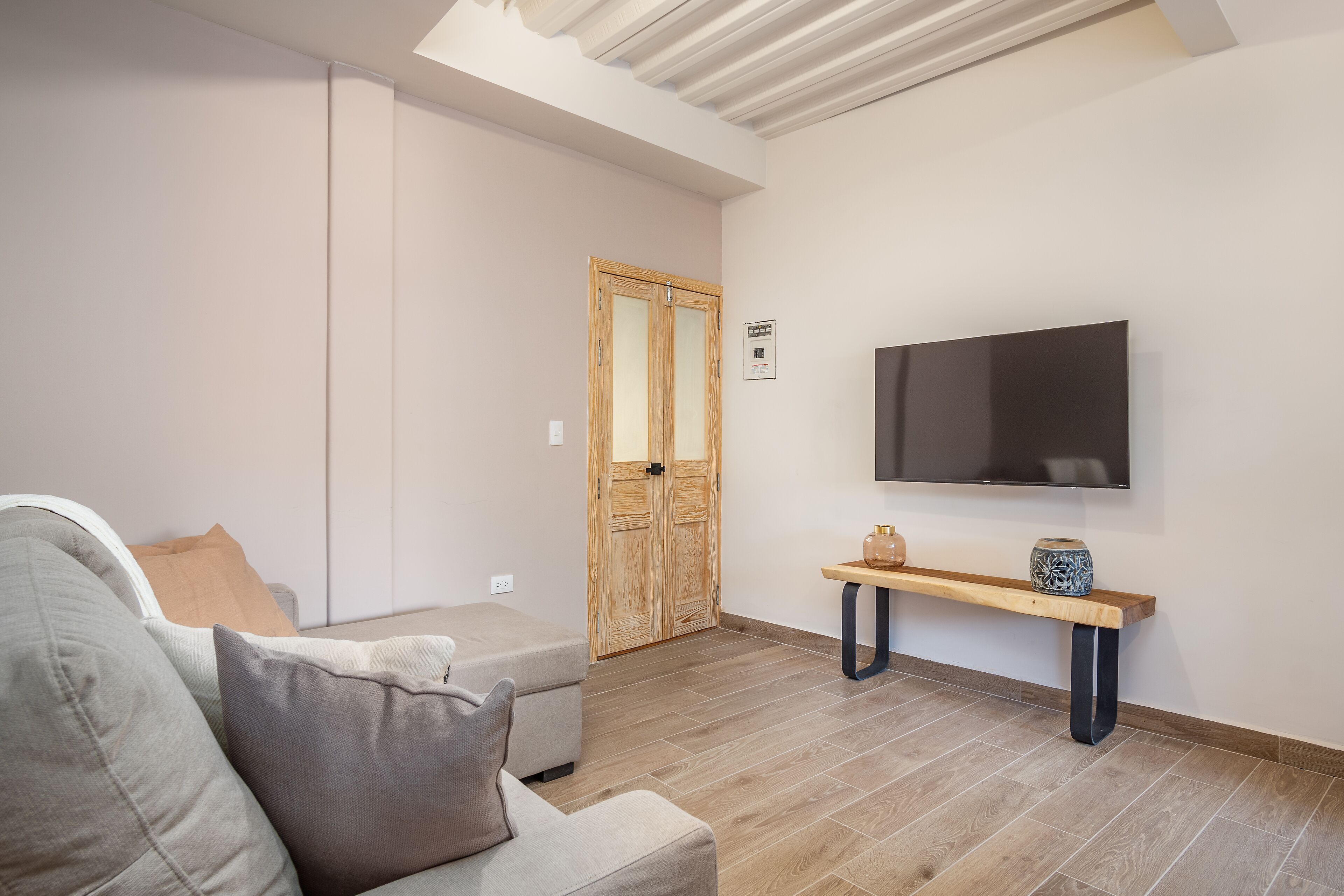 Een moderne woonkamer met een bank, een aan de muur bevestigde televisie en een houten deur op de achtergrond.