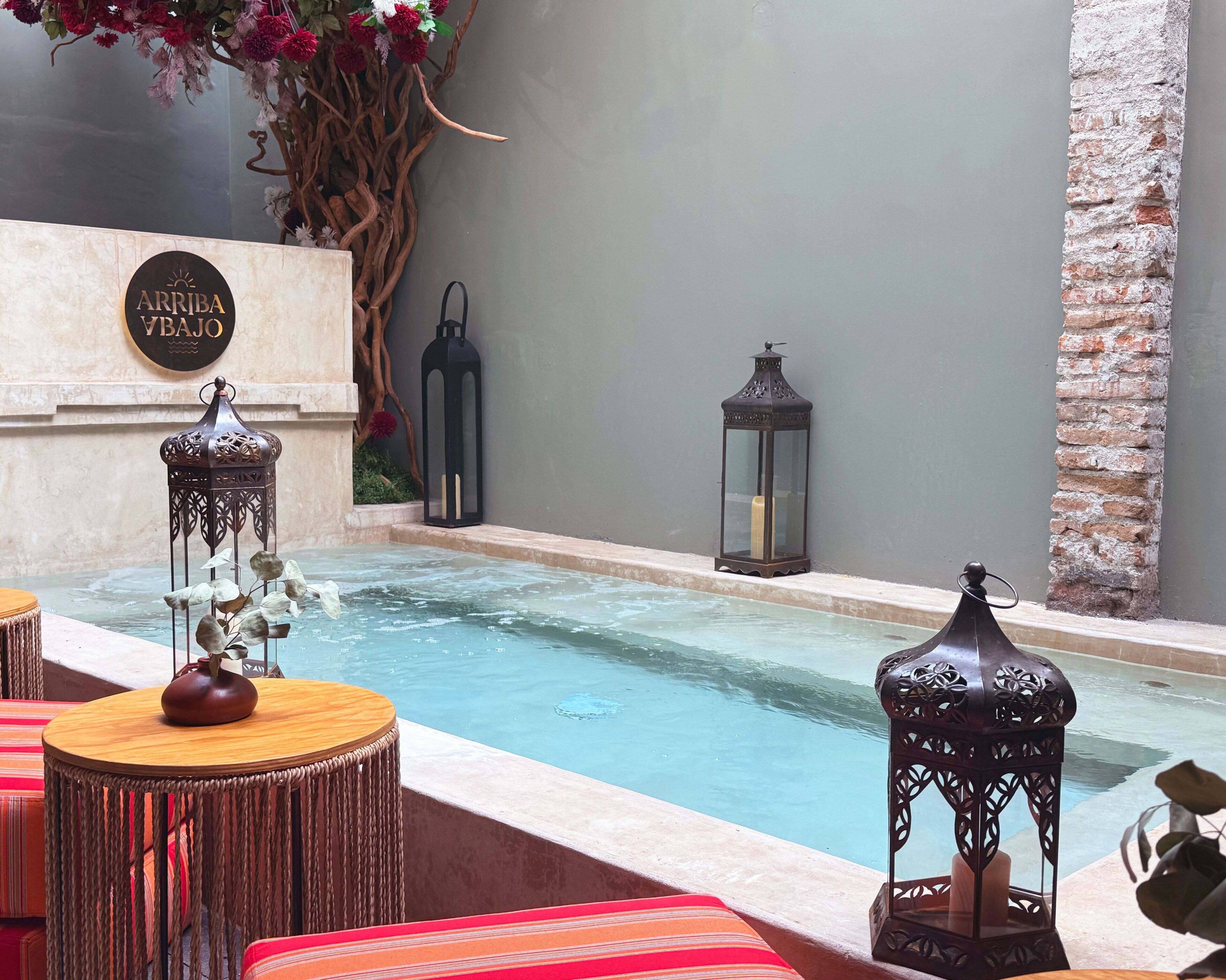 A pool area with a stone wall, decorative lanterns, and a sign that reads "ARRIBA YABAJO".