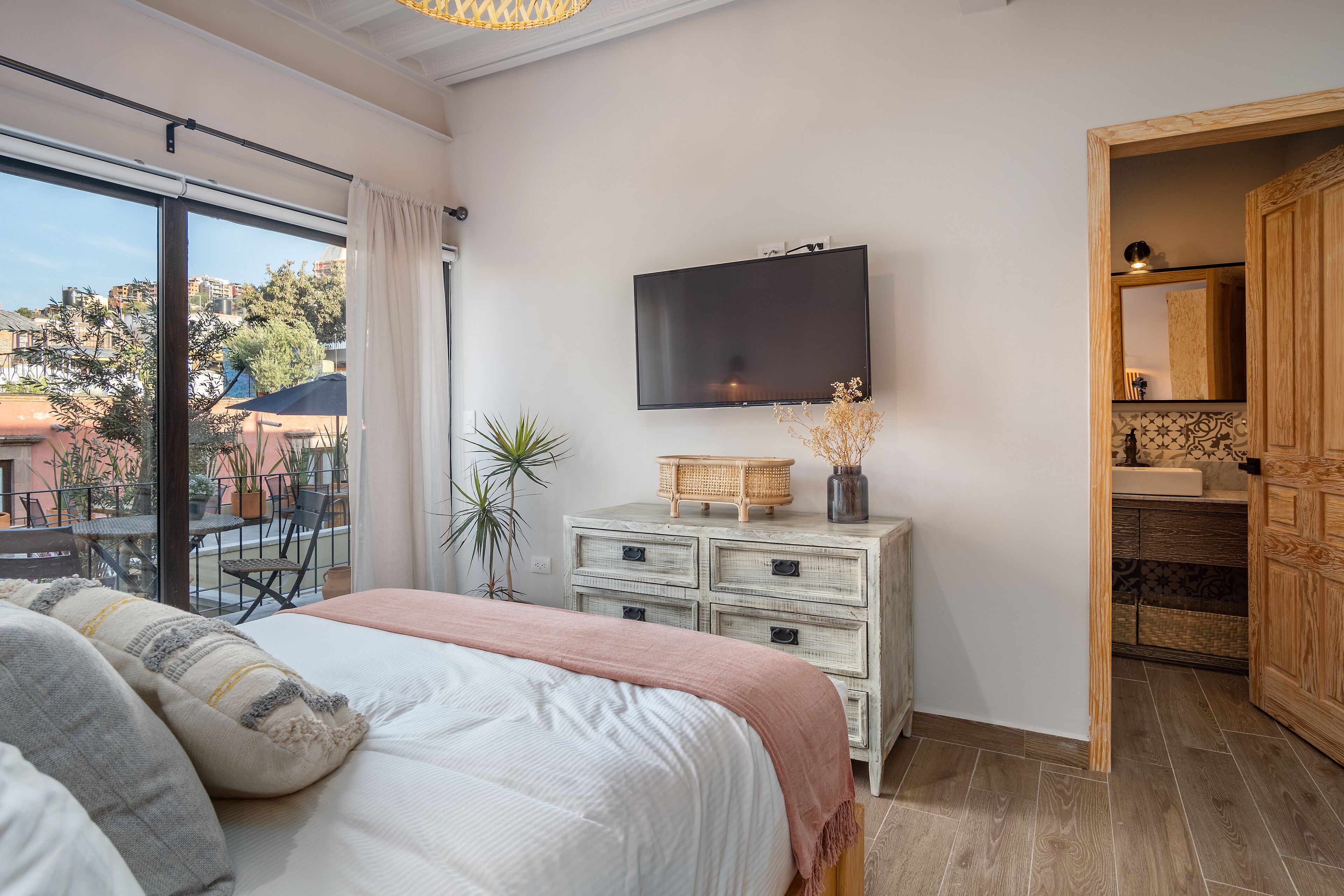 A bedroom with a large bed, a television on the wall, a dresser, and a view of the outside balcony.