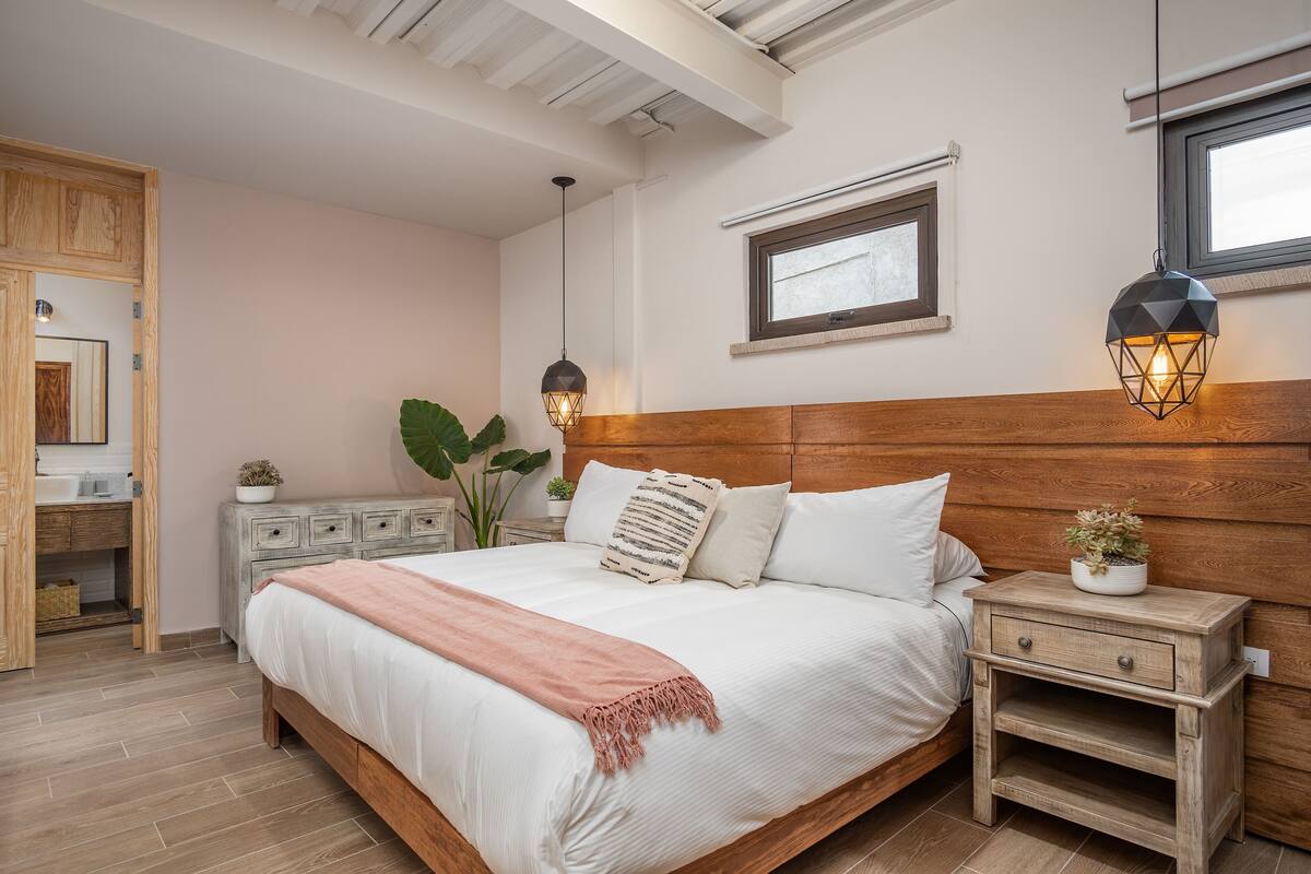 Een slaapkamer met een houten hoofdbord, een nachtkastje met een plant en een raam met uitzicht.