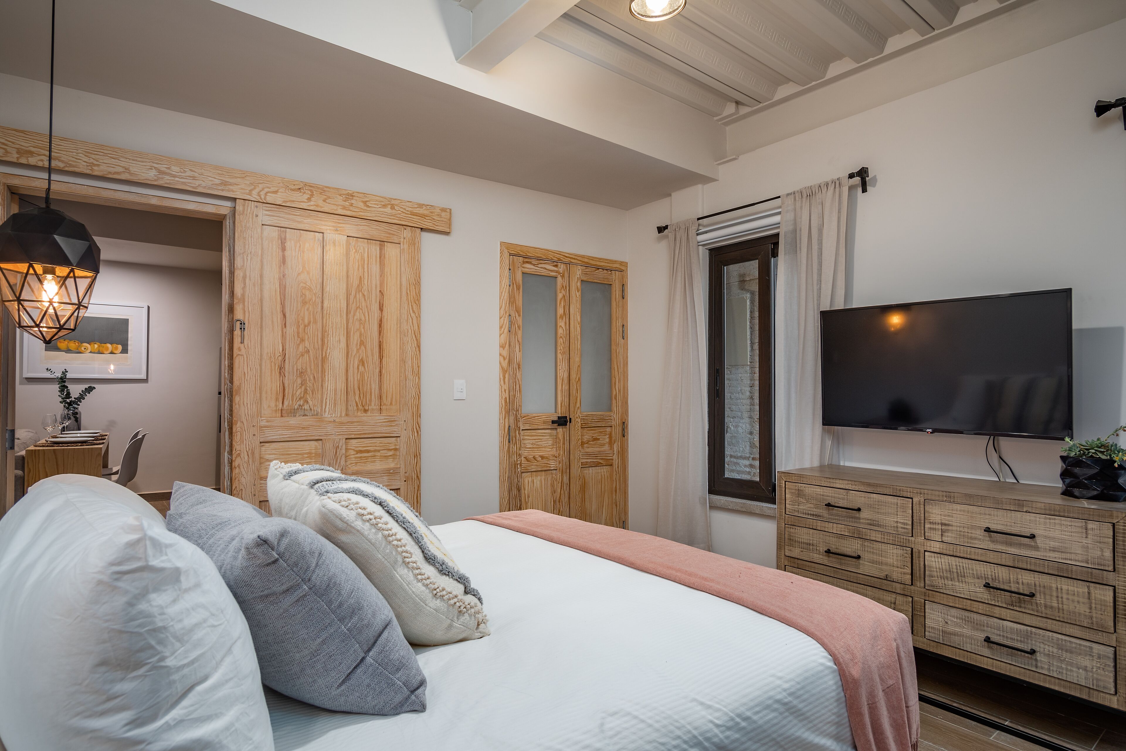 Quarto com cama, guarda-roupa de madeira, televisão e luminária pendente.