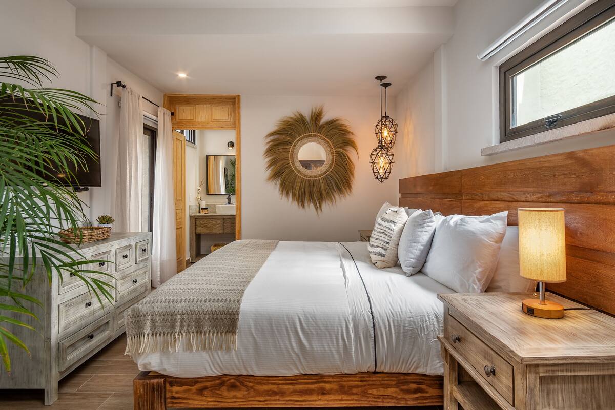Een slaapkamer met een bed, nachtkastje, lamp en een grote spiegel aan de muur.