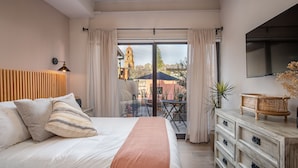 A bedroom with a large bed, a TV, a wooden headboard, a dresser, and a balcony with a view of a building and plants. - Casa Pandurata Luxury Apartments in Centro, San Miguel de Allende (San Miguel de Allende)