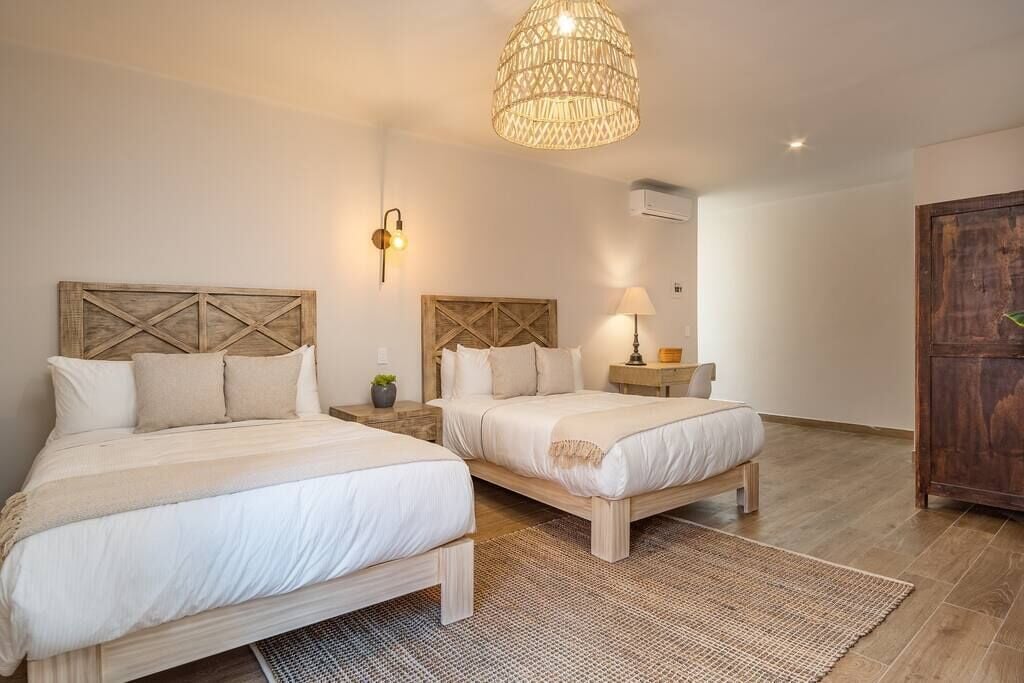 A bedroom with two beds, a woven light fixture, a wall-mounted lamp, and a wooden wardrobe.