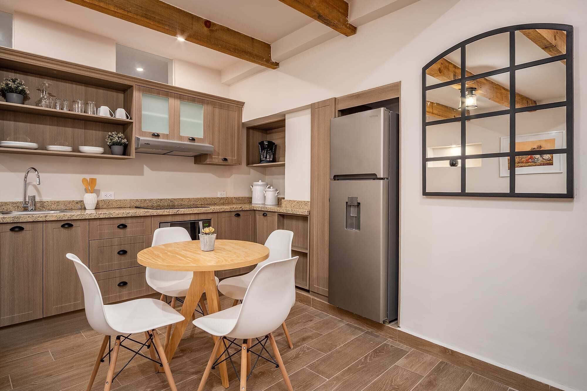 A modern kitchen with wooden cabinets, a stainless steel refrigerator, and a round dining table with white chairs.