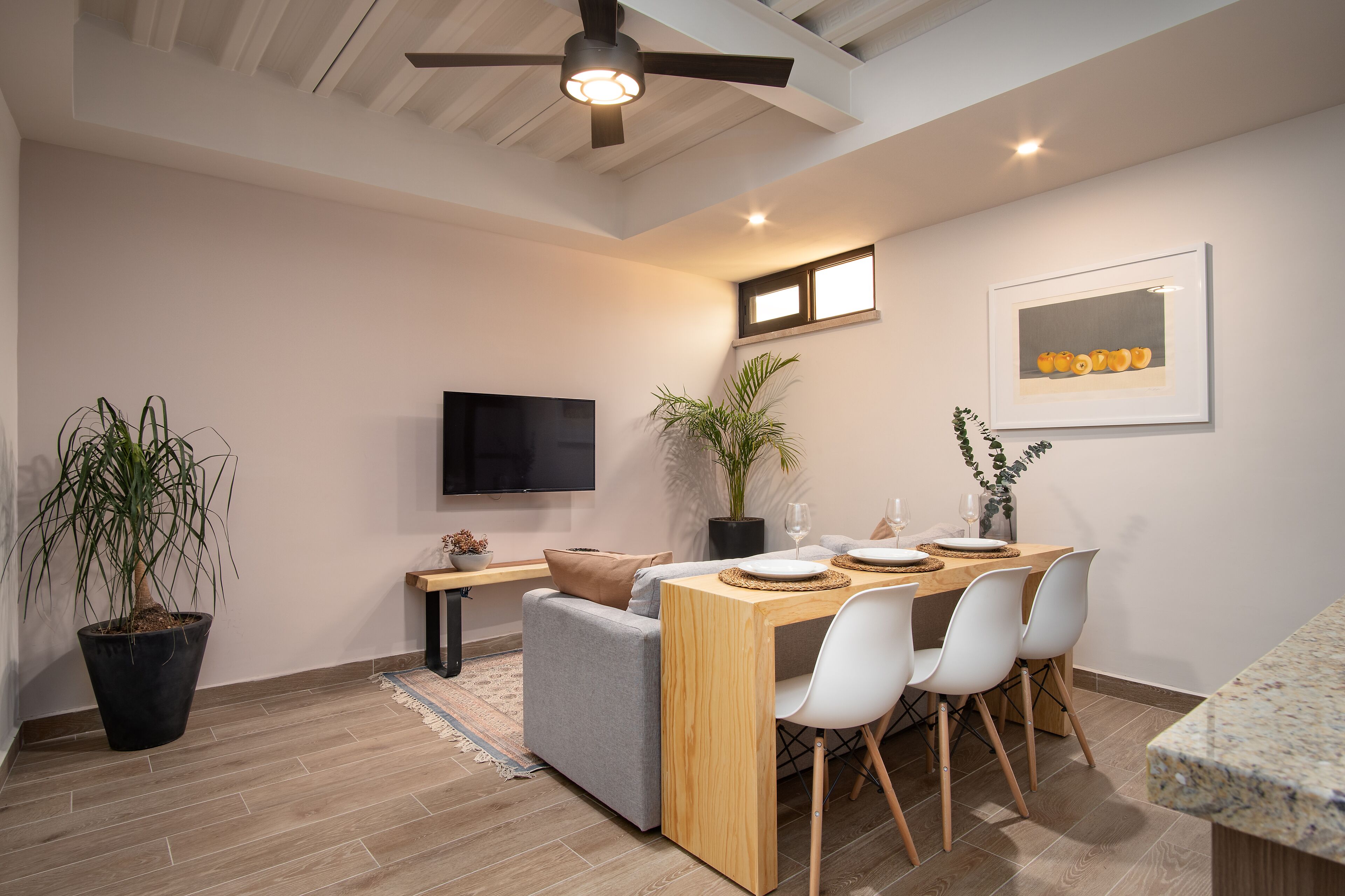 A modern living room with a sofa, dining table, chairs, a TV, and a ceiling fan.