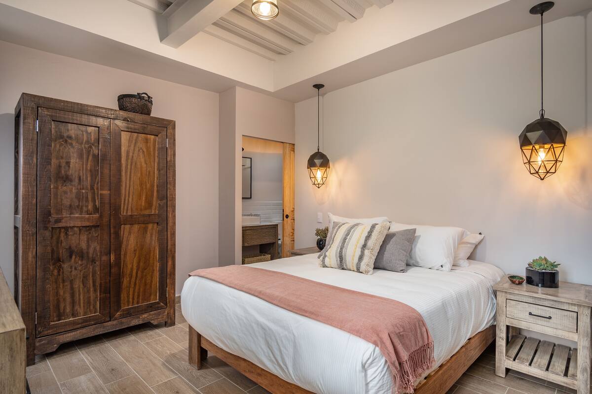 Een slaapkamer met een houten bed, een nachtkastje, een kledingkast en twee wandlampen.