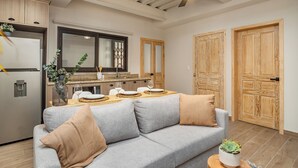 A modern kitchen with a built-in refrigerator, a dining area with a wooden table and chairs, and a grey sofa with cushions. - Casa Pandurata Luxury Apartments in Centro, San Miguel de Allende (San Miguel de Allende)