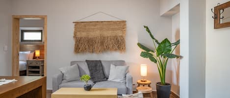 A cozy living room with a grey sofa, a wooden coffee table, a hanging woven tapestry, a potted plant, and a small side table with a lamp.