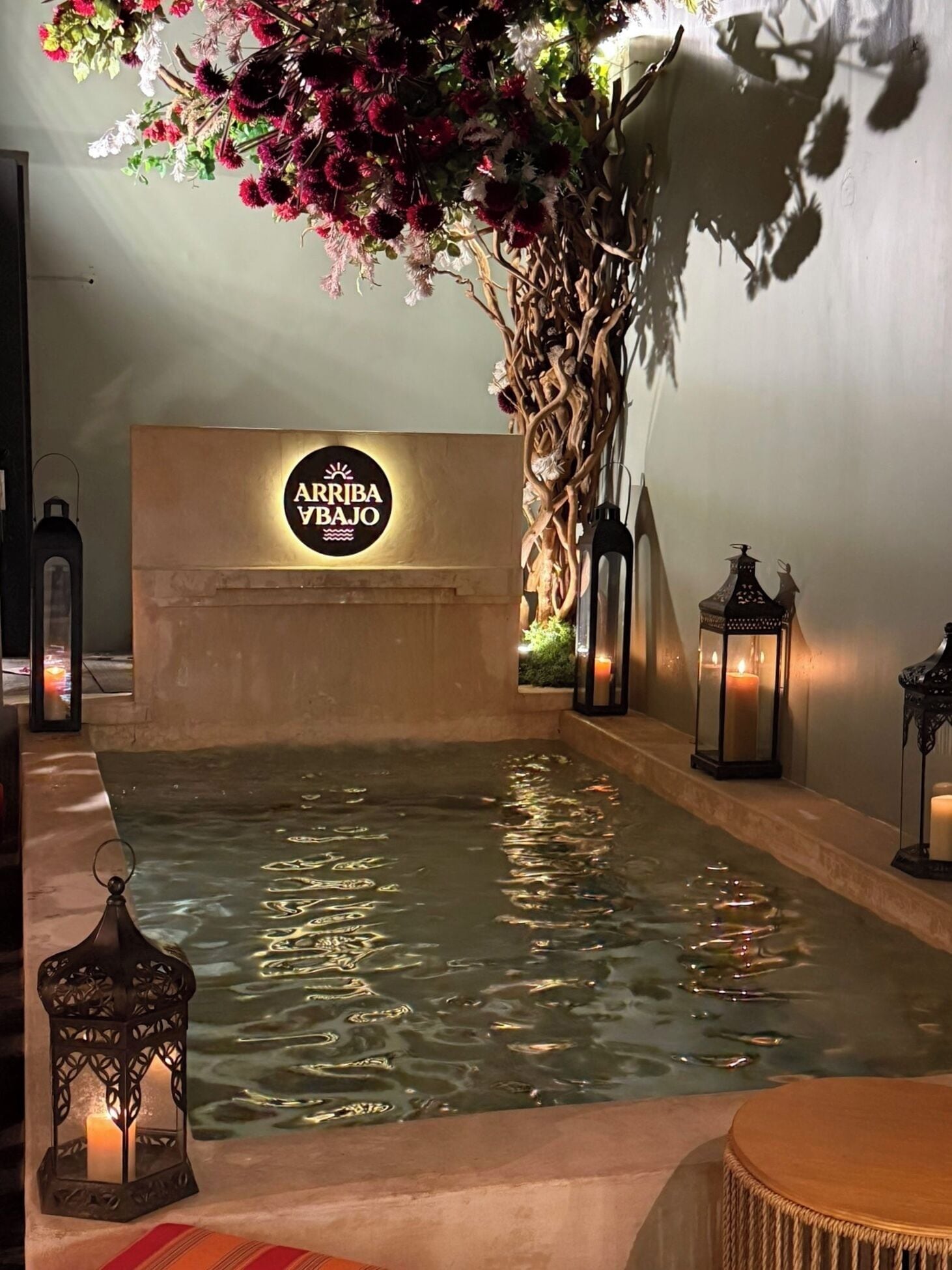 A spa area with a water feature, a wall-mounted sign reading "ARRIBA BAJO", and decorative lanterns.