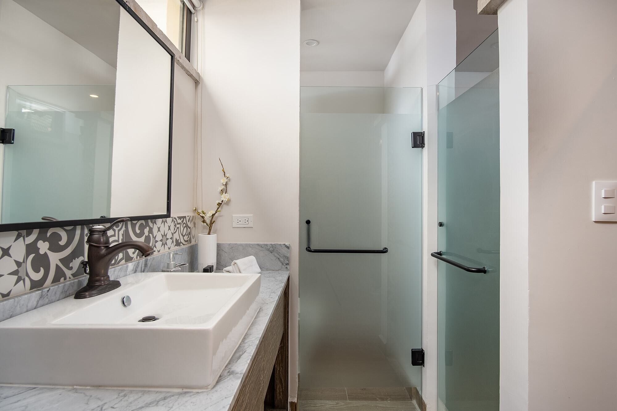 Un baño moderno con un espejo grande, un lavabo blanco y una cabina de ducha de vidrio.