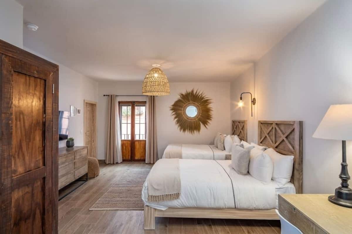 Een slaapkamer met twee bedden, een houten garderobe, een grote spiegel en een hanglamp.