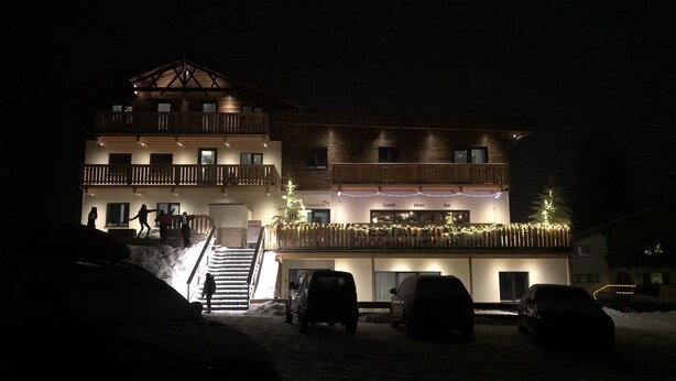 Un edificio de varios pisos con una escalera que conduce a los pisos superiores, un comedor con un árbol de Navidad y varios coches aparcados en la parte delantera.