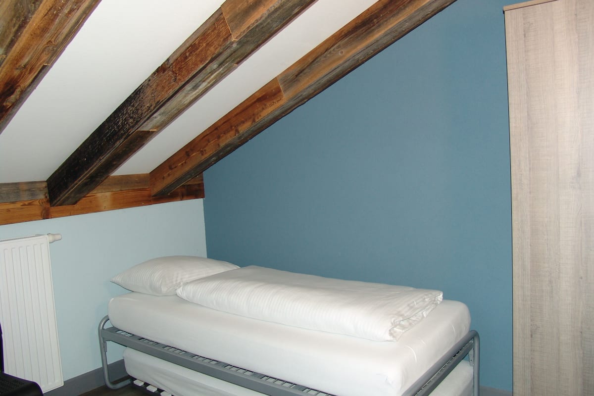 Un letto singolo in una stanza con soffitto spiovente e travi a vista in legno.