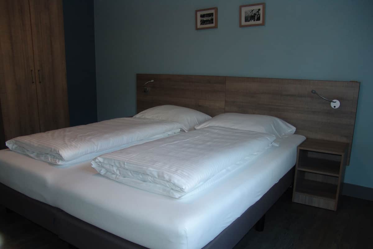 Un letto matrimoniale con lenzuola bianche in una stanza con una testiera in legno e un comodino.