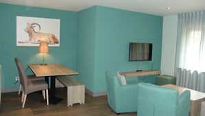 Una sala de estar moderna con paredes verde azulado, una mesa de comedor de madera, un sofá y un televisor instalado en la pared.