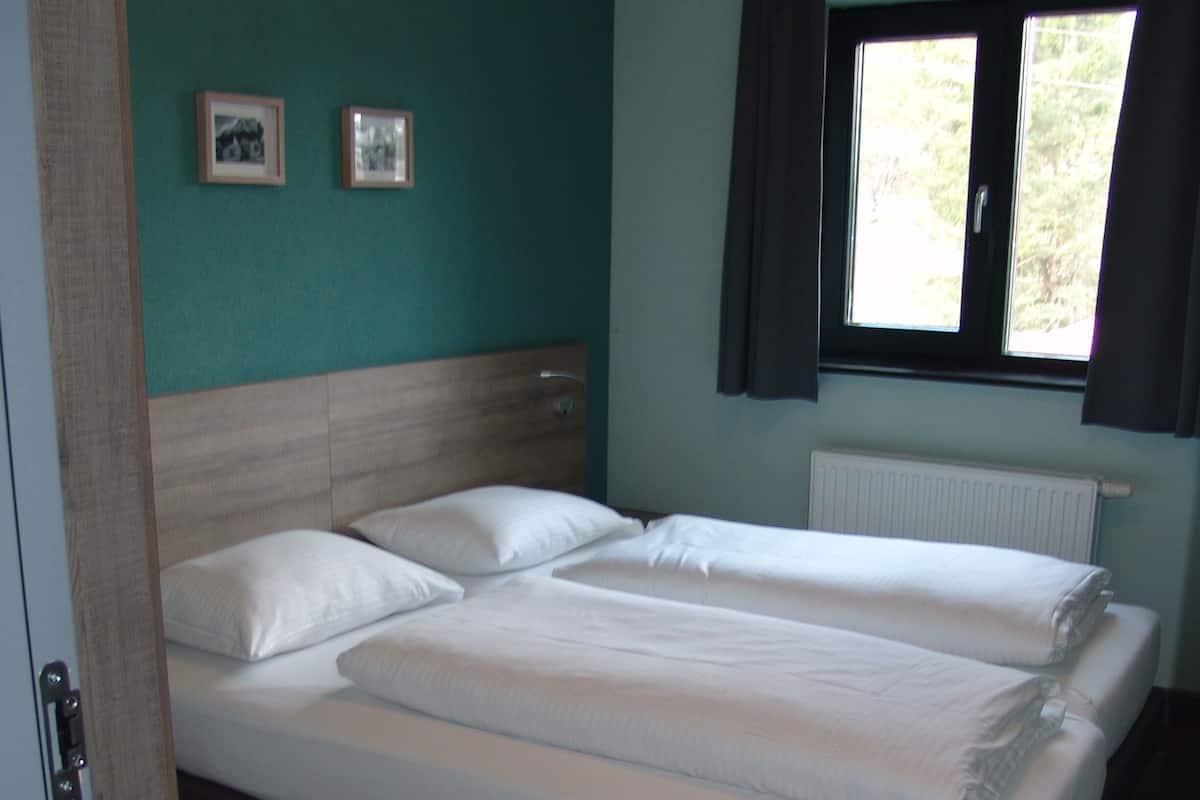Un letto matrimoniale con lenzuola bianche, una testiera in legno, una finestra con tende e un termosifone.